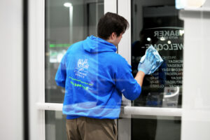 Man in blue shirt and blue gloves wiping down glass doors with blue towel